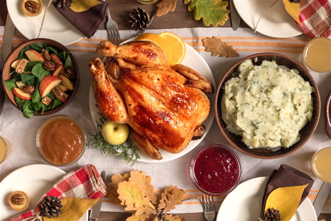 An assortment of holiday foods such as turkey, mashed potatoes, gravy, cranberry sauce on table.