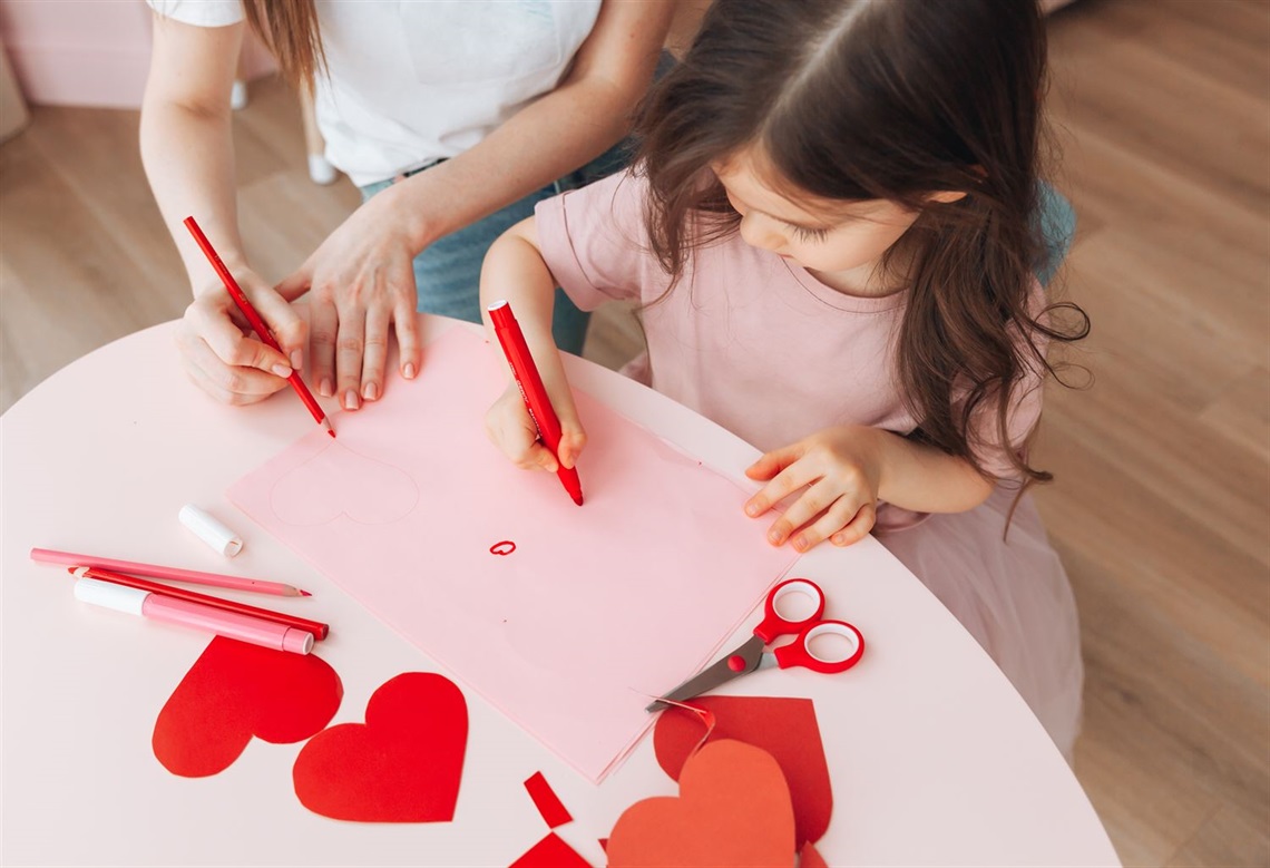 Young girl drawing with a red marker on a Valentine's craft