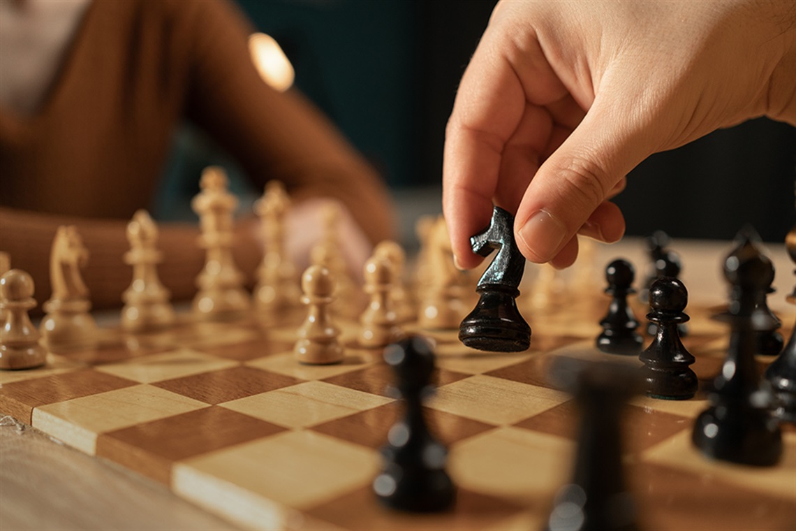 Close-up shot of a hand moving a black chess piece during a game between two players.
