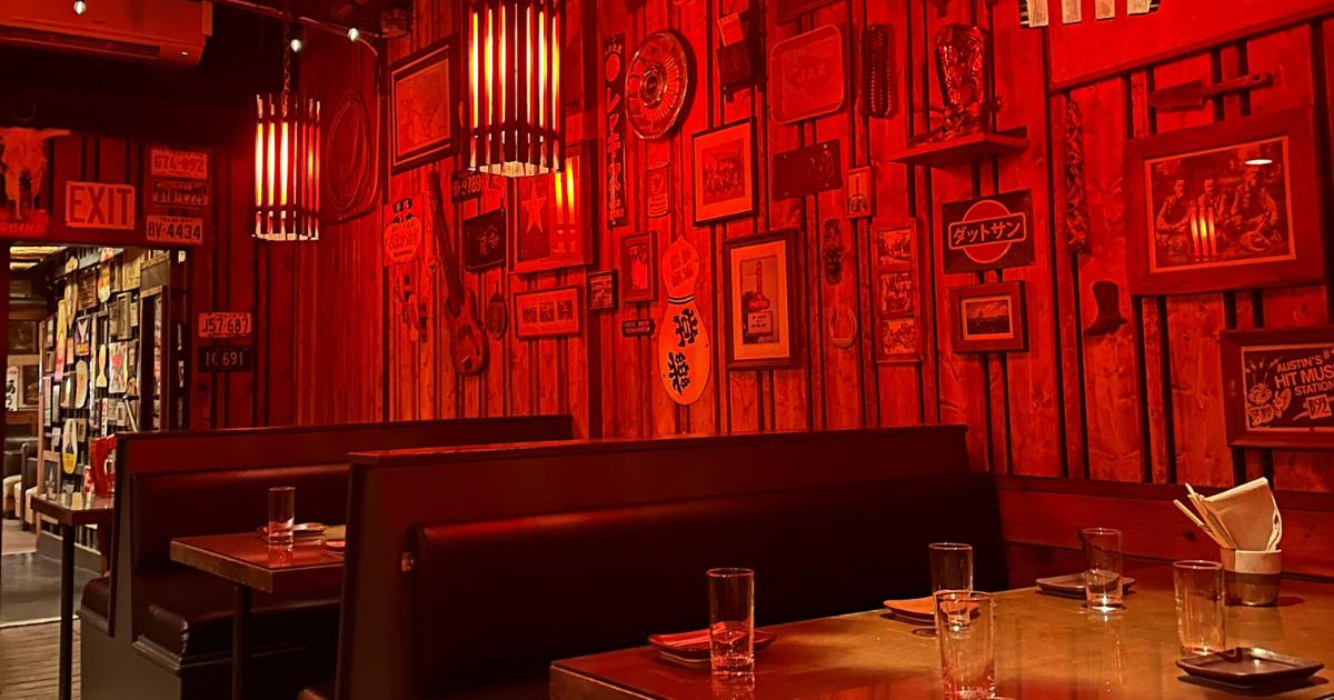 Interior at Kemuri Tatsu-ya in Austin, Texas. Two booths and red lights and decor, with lots of Asian dive-bar style framed signs on the walls.