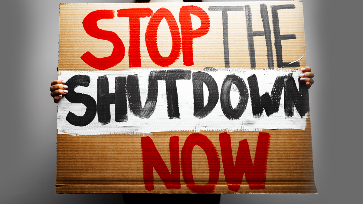 A photo illustration of a person holding a cardboard sign with the words "Stop the Shutdown Now."