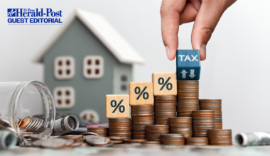 A photographic illustration of property taxes showing a stack of coins in front of a toy house.