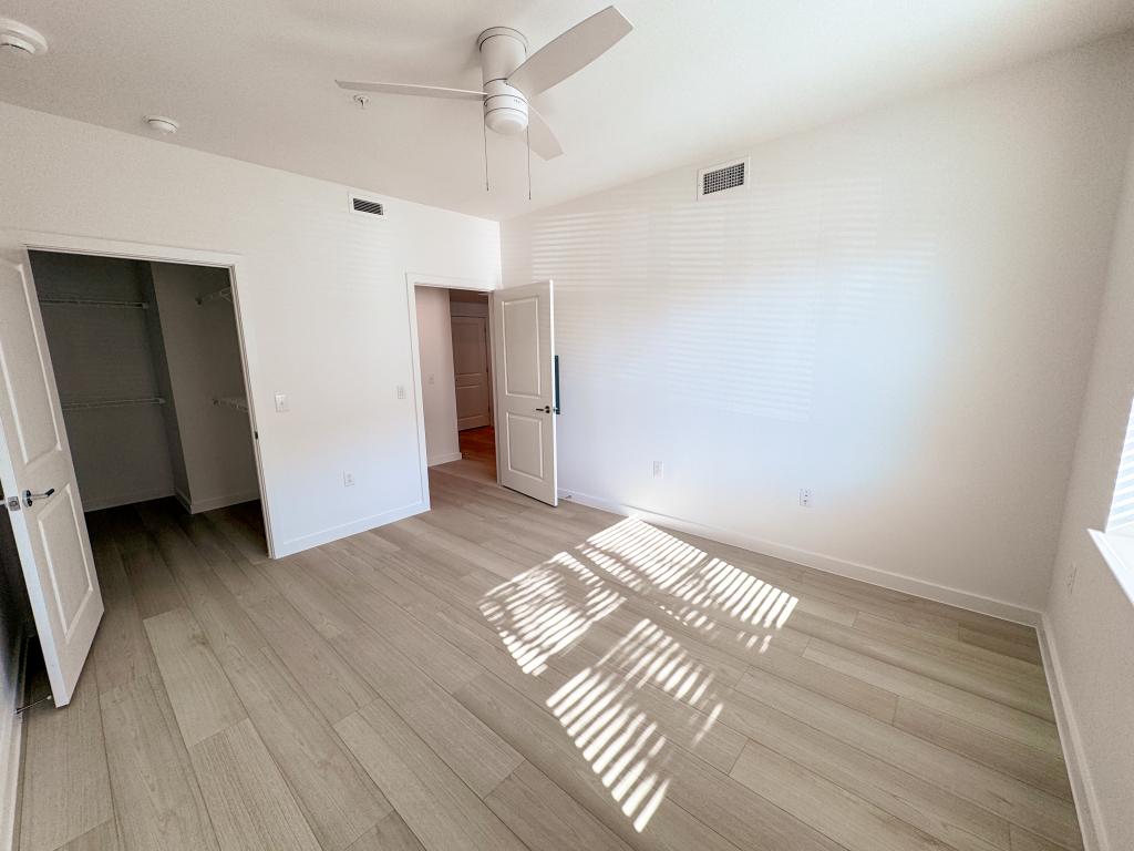 Bright bedroom with ceiling fan, open closet, and wood floors.