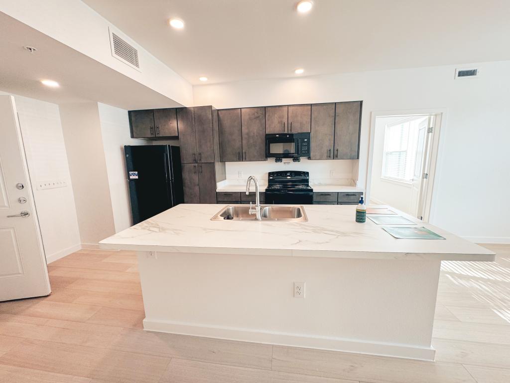 Open kitchen with quartz island, dark cabinets, and black appliances.