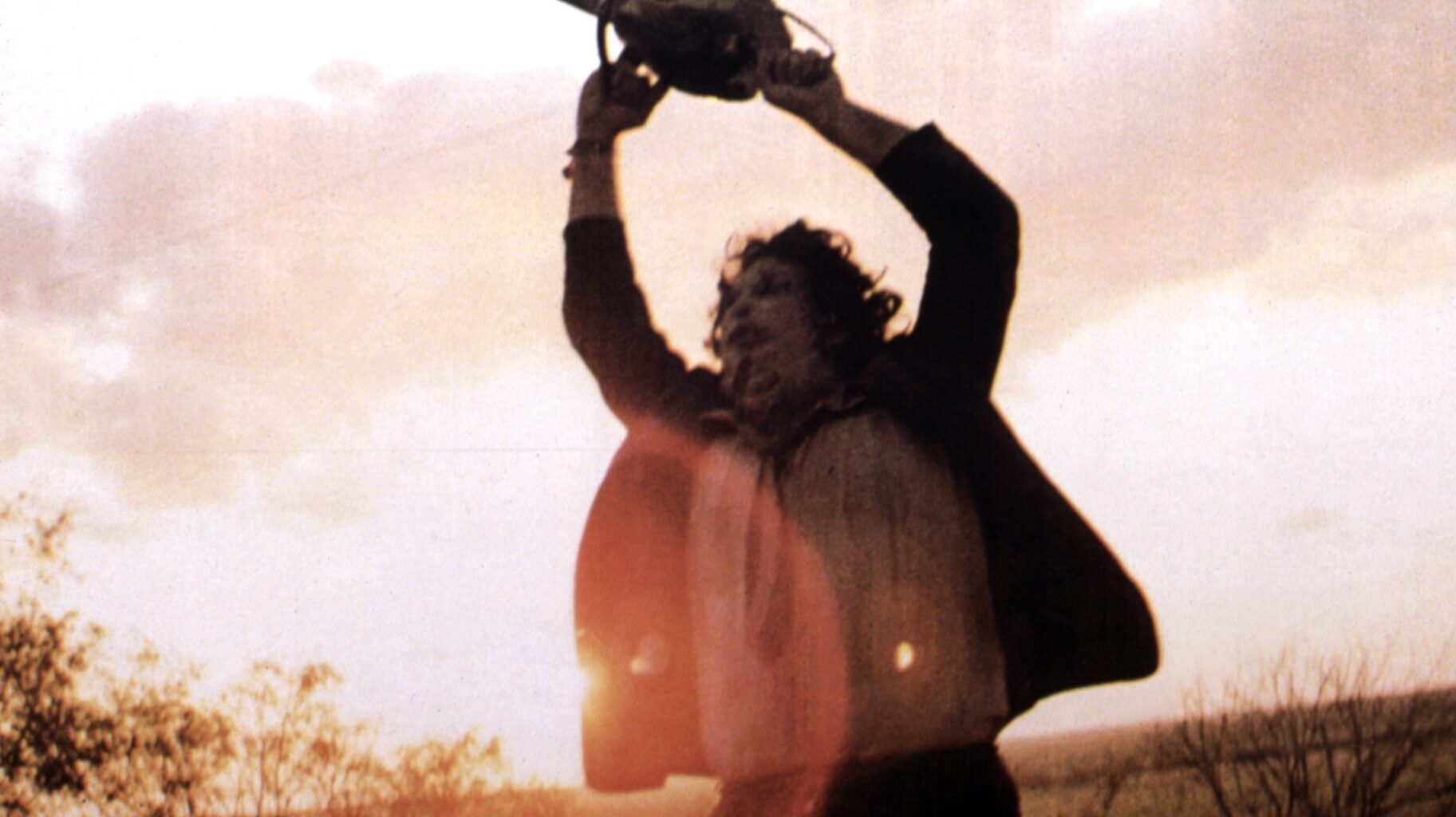 Leatherface (Gunnar Hansen) holds a chainsaw above his head in The Texas Chain Saw Massacre (1974).