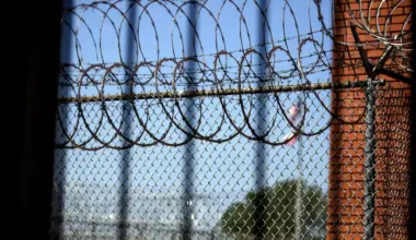 The red brick walls and barbed wire of the Huntsville Unit, a state prison, are visible through a fence.