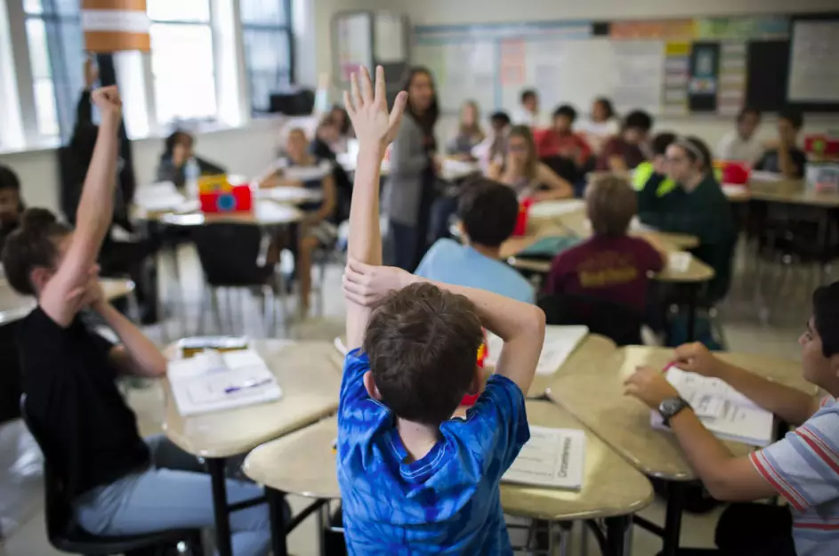 Elementary school students in a Texas classroom raise their hands