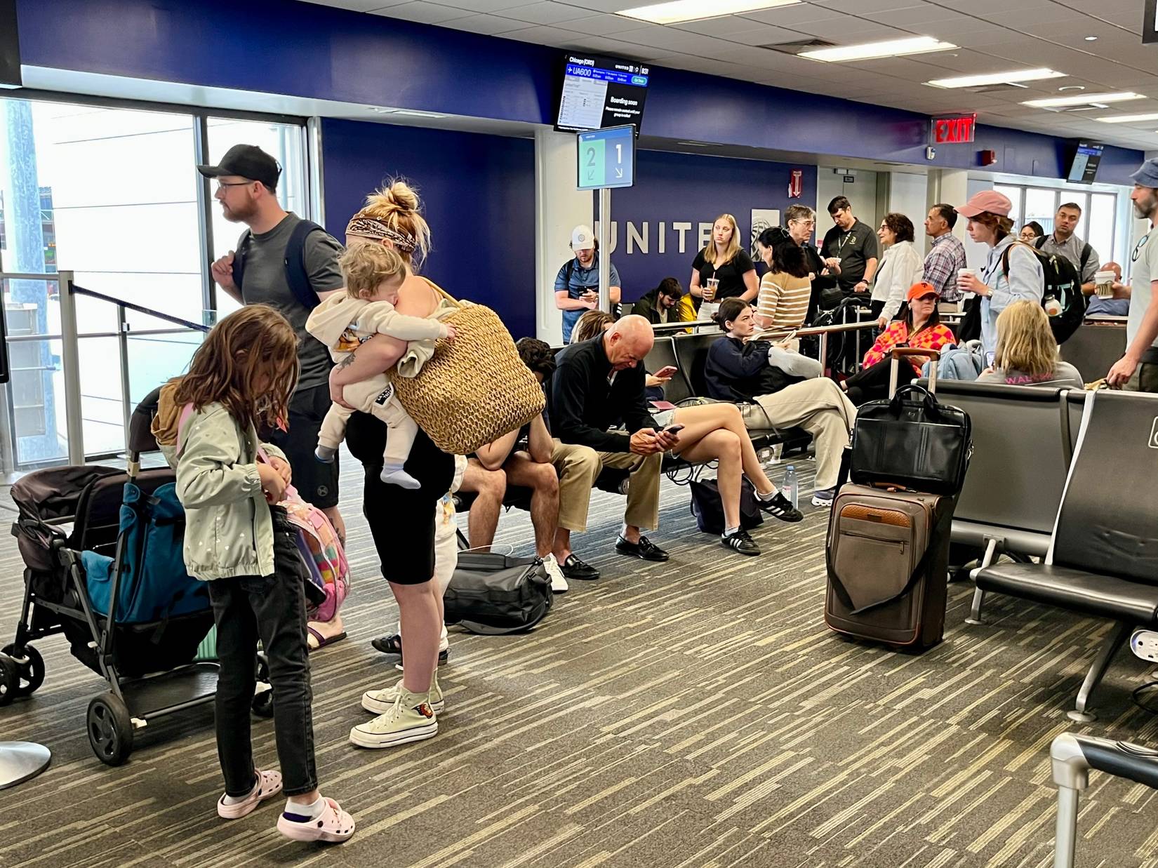 United Airlines Passengers waiting to board a flight at the gate. Some are standing while others are sitting.