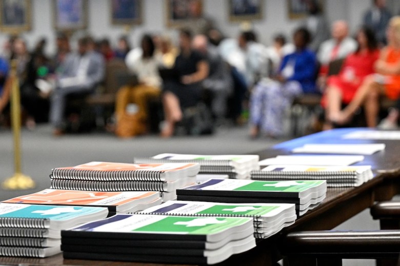 State Board of Education meeting attendees listen to the discussion as school workbooks span a table across the room on June 26, 2024 at the William B. Travis Building in Austin.