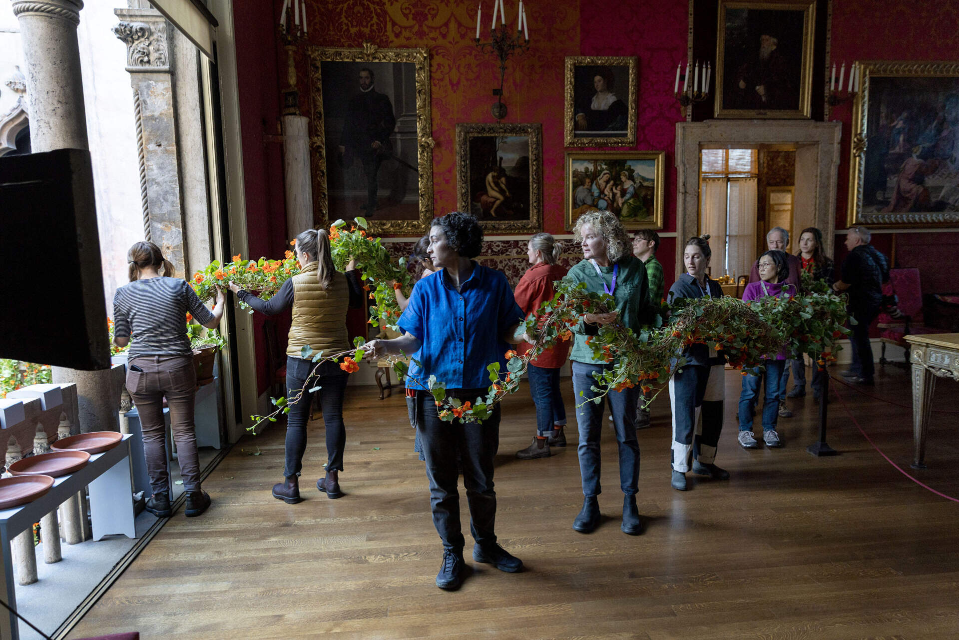 Members of the museum’s horticulture team and volunteers move nasturtium vines through the Titian Room and out of one of the windows into the courtyard at the Isabella Stewart Gardner Museum. (Robin Lubbock/WBUR)