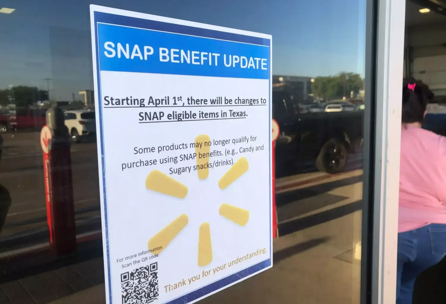 A sign outside a Walmart that reads "SNAP benefit update: Starting April 1, there will be changes to SNAP eligible items in Texas. Some products may no longer qualify for purchase using SNAP benefits (e.g. Candy and Sugary snacks/drinks)." The text is over the Walmart logo, which includes six yellow shapes that look like flower petals arranged in a circle. The sign also includes a QR code and the words "Thank you for your understanding!" at the bottom in yellow text.