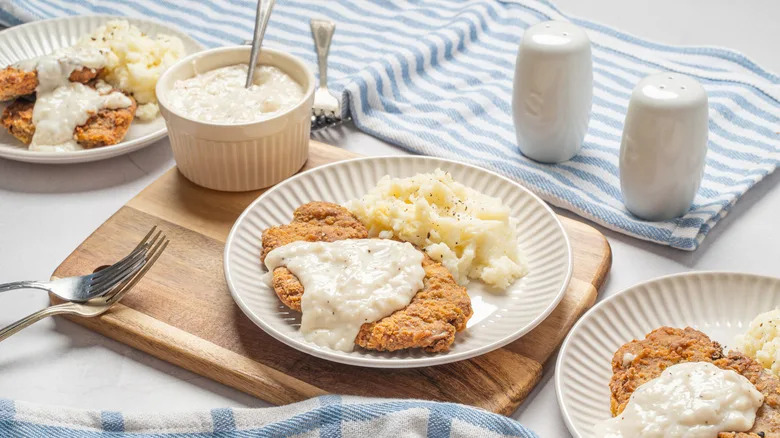 Homemade chicken-fried steak on white plates with mashed potatoes.