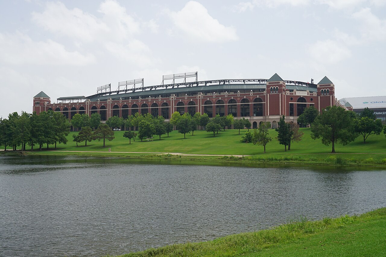 Choctaw Stadium across a small body of water surrounded by green grass.