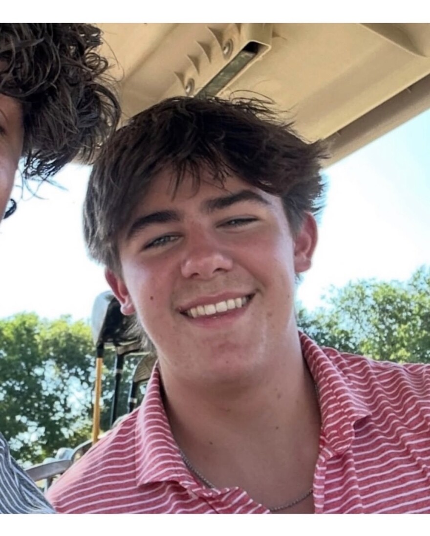 A close-up photo of a smiling young man in a red striped shirt.