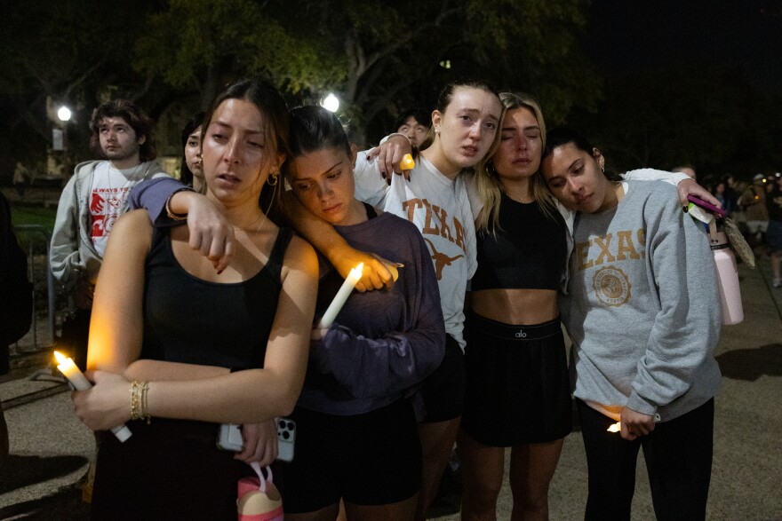 Four young women lean on each other as they hold candles at a candlelight vigil.