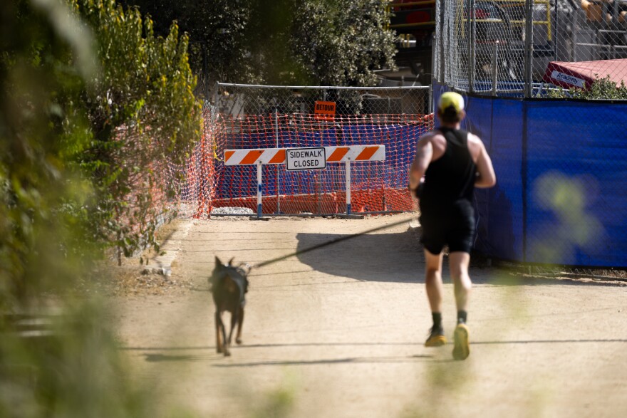 A man runs with their dog towards a sidewalk closure sign on Lady Bird Hike and Bike trail on Tuesday, Oct. 21, 2025. 