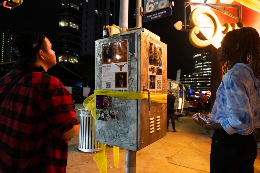 People stop to look at flyers with information on the shooting victims that are attached to an box on a city sidewalk.