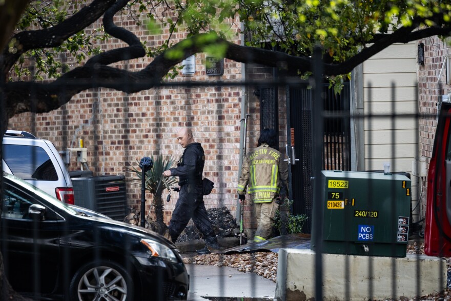 A firefighter and arson investigator are seen through a metal fence walking near the entry point to an apartment which had suffered a fire.
