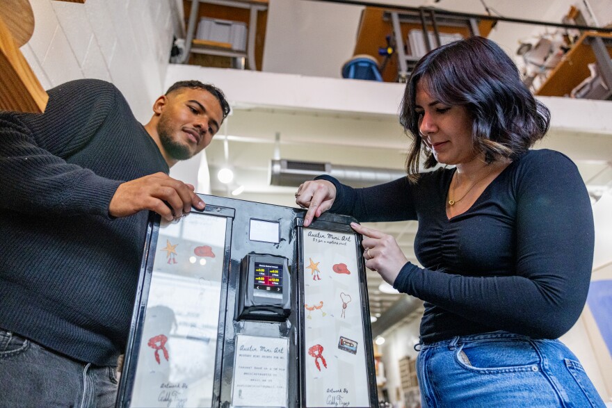 A man and woman are shown near a small vending machine touching the buttons. 