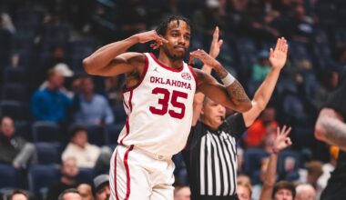 OU's Tae Davis in red uniform goes up for a layup against a Texas A&M defender in white uniform as players from both teams look on, in the SEC Tournament at Bridgestone Arena in Nashville, Tenn.