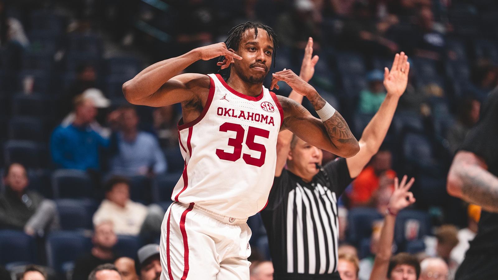 OU's Tae Davis in red uniform goes up for a layup against a Texas A&M defender in white uniform as players from both teams look on, in the SEC Tournament at Bridgestone Arena in Nashville, Tenn.