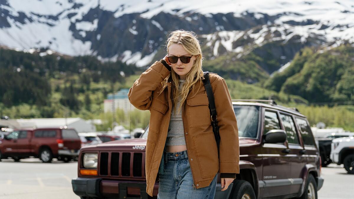 A woman in shades walks in a parking lot in a mountain town.