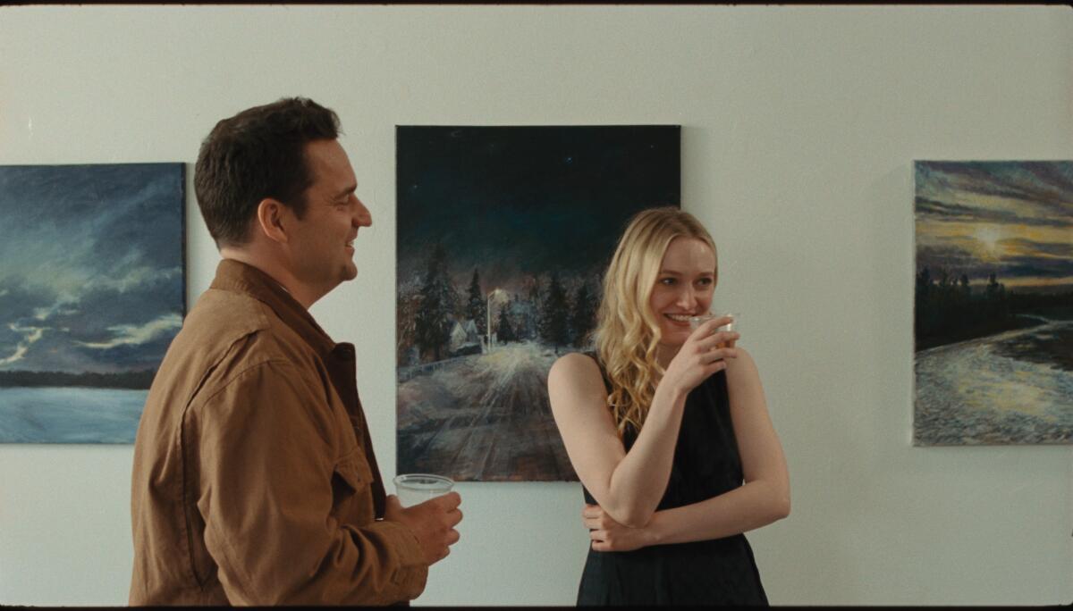 Two people laugh in a room with art hanging in it.