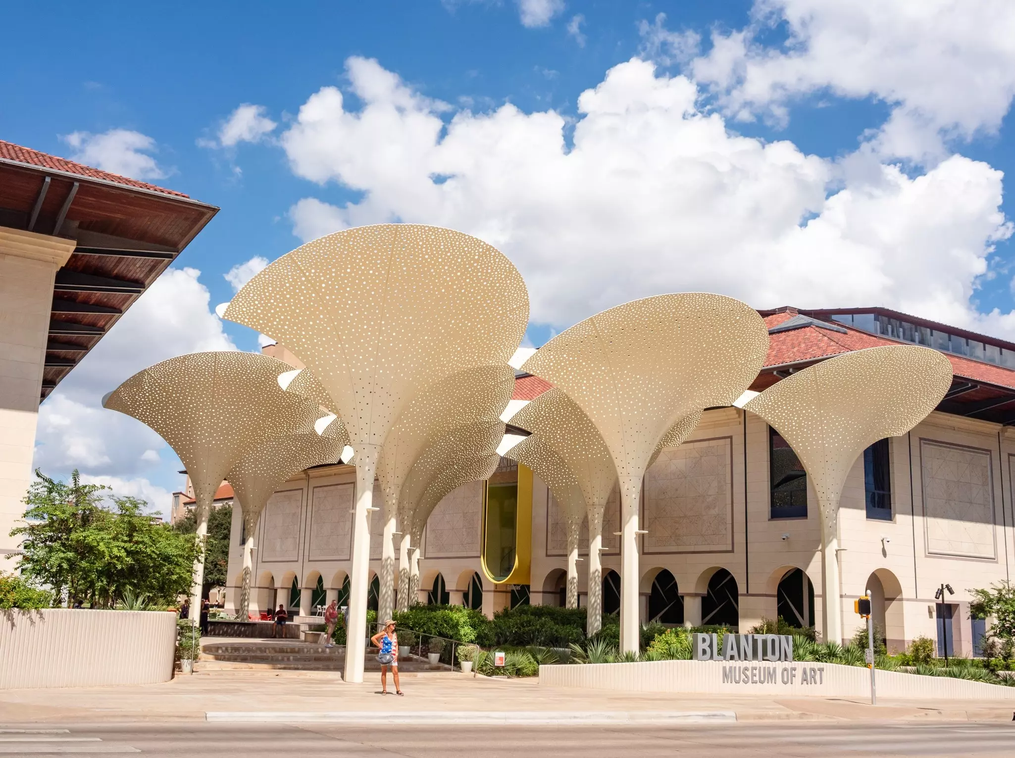 A woman stands in front of fan-topped columns in front of a modern museum building.