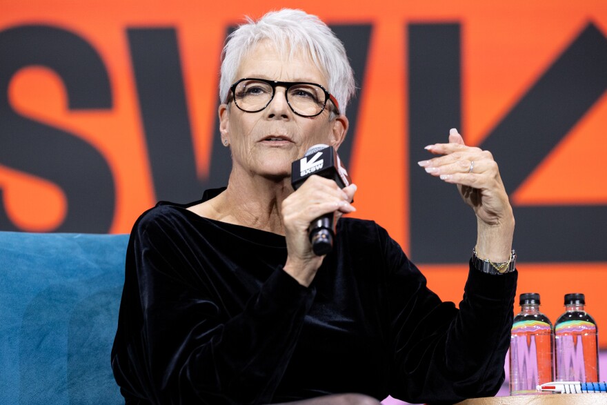 Jaime Lee Curtis speaks into a SXSW branded microphone on a stage.