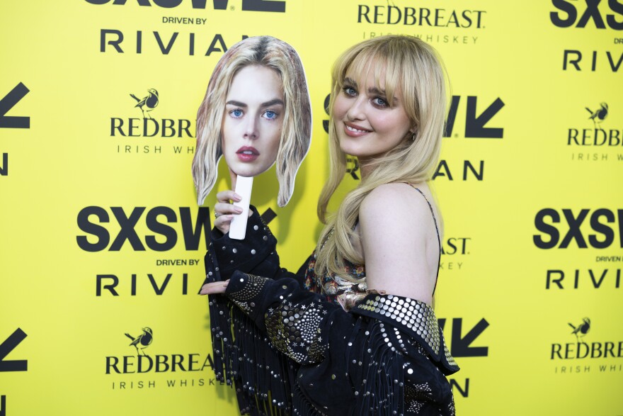 Kathryn Newton poses for photos with a cutout of lead actress Samara Weaving’s head in front of a yellow backdrop with SXSW logos on it.