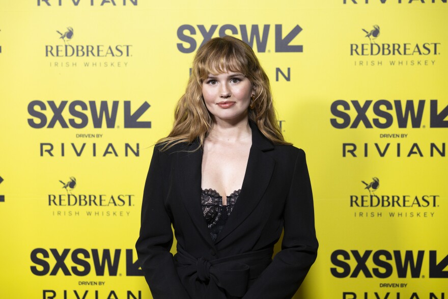 Debby Ryan stands in front of a yellow backdrop with SXSW logos on it.