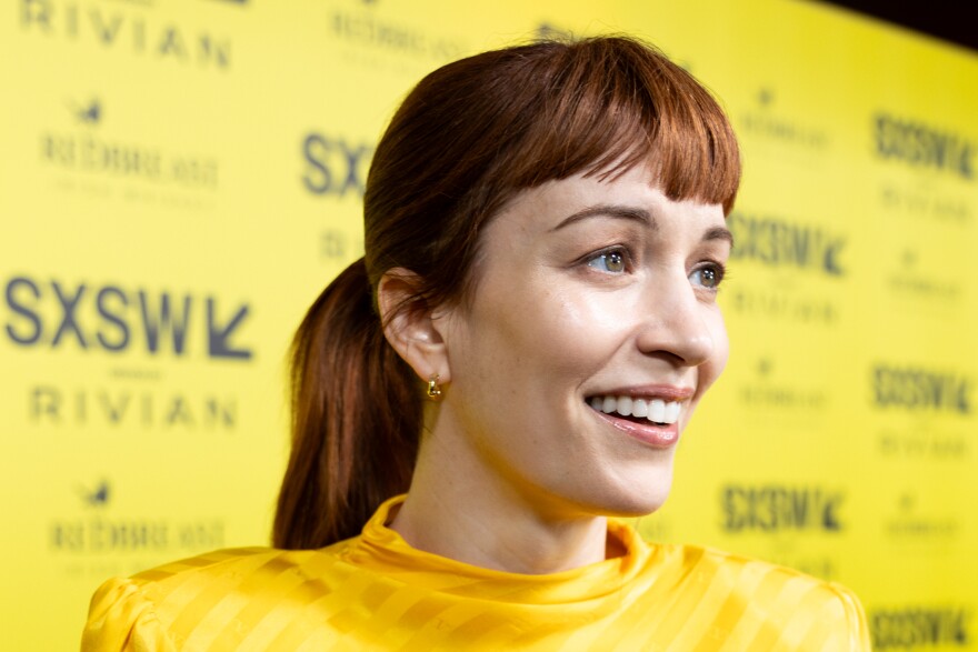 Britt Lower smiles in front of a yellow backdrop with SXSW logos on it.