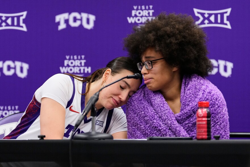 TCU's Marta Suarez, left, wears a white TCU jersey and leans her head on Olivia Miles' shoulder, right, who is wrapped in a purple sherpa blanket. They both sit behind a table with a microphone in the foreground after an NCAA women's basketball game against Arkansas Pine Bluff in Fort Worth, Texas, Tuesday, Dec. 16, 2025.
