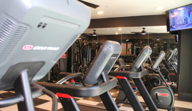 Image shows new fully equipped gym, complete with weight machines and a row of treadmills and bikes. The far wall is lined with mirrors.