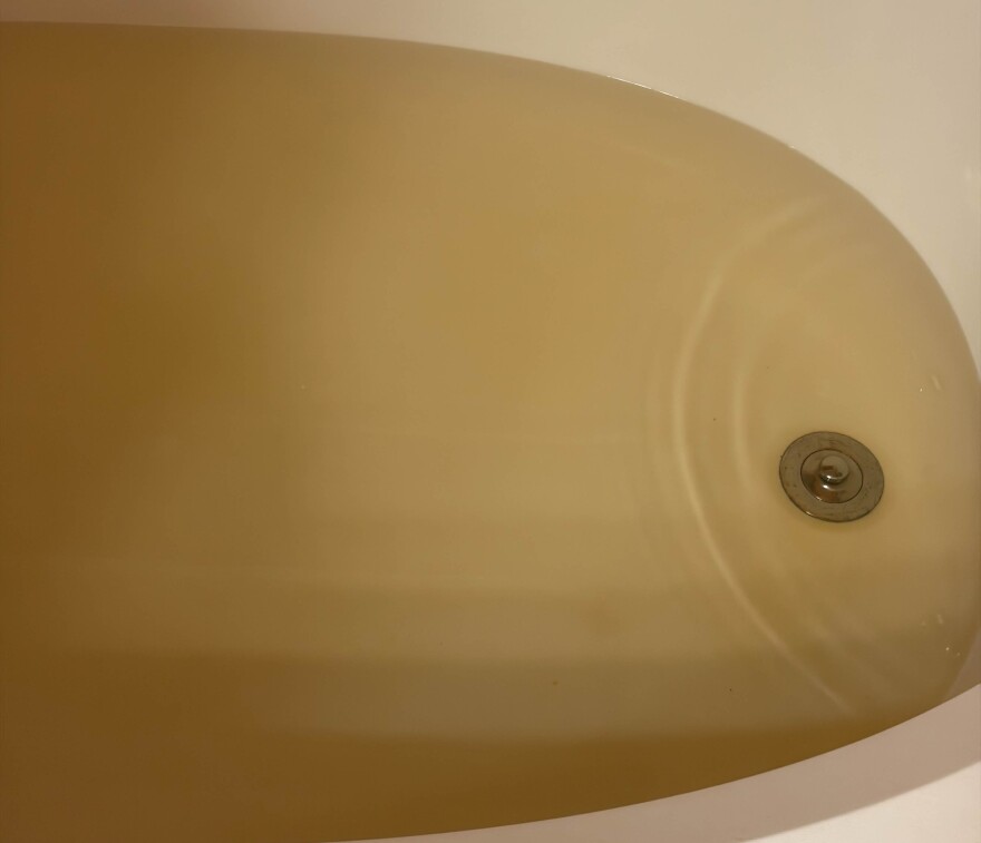 A bathtub filled with brownish/yellow water. 