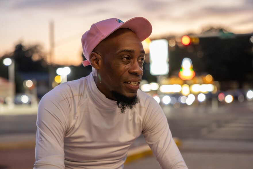 A man wearing a hat and brightly colored clothing sits for a portrait at an intersection.