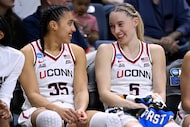 UConn guards Azzi Fudd (35) and guard Paige Bueckers (5) smile at each other on the bench in...