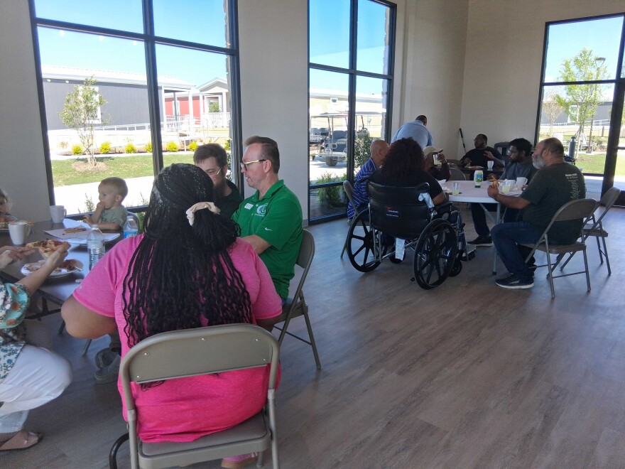Women, men and children of various ages gather to eat lunch. They are sitting in chairs. One woman is in a wheelchair. 