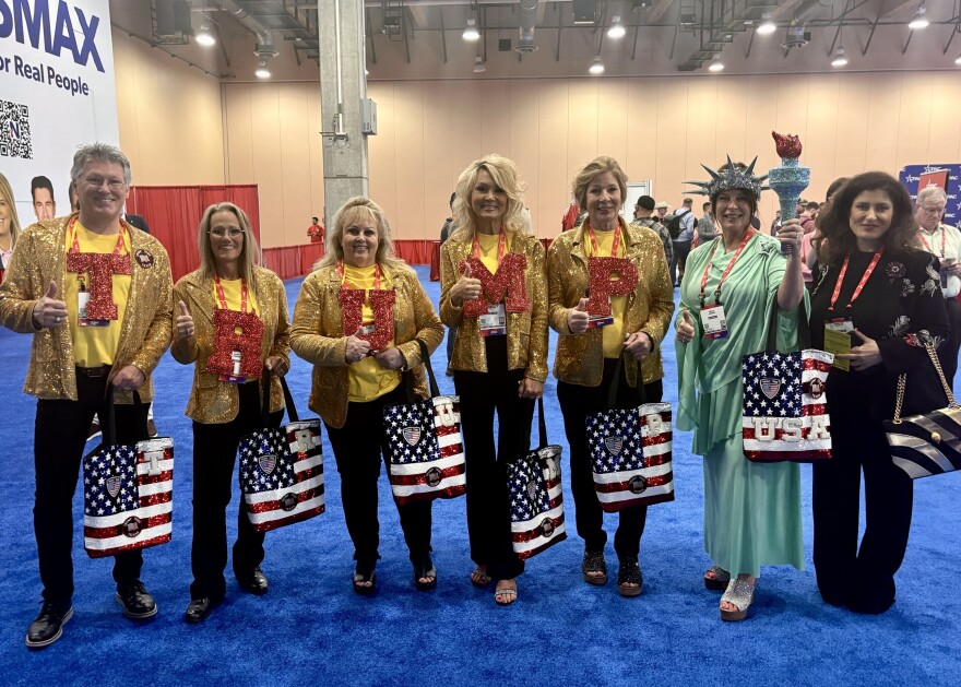 The Trump Tribe of Texas poses for a photo at CPAC, wearing gold jackets with bold, bedazzled red letters spelling “TRUMP,” while one member is dressed as the Statue of Liberty.