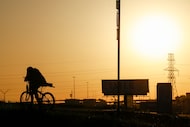 A man walks his bike over the Beach Street bridge at Interstate 30 as the sun sets,...