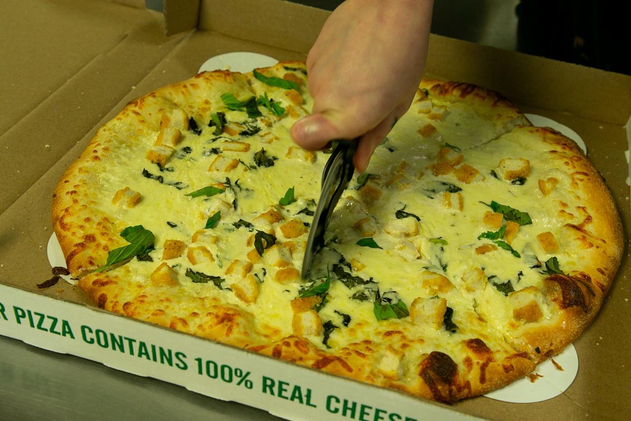 Kylie Painter, a pizzaiolo at Authentic New York Pizza, slices up a chicken Alfredo pizza on Feb. 8, 2023.