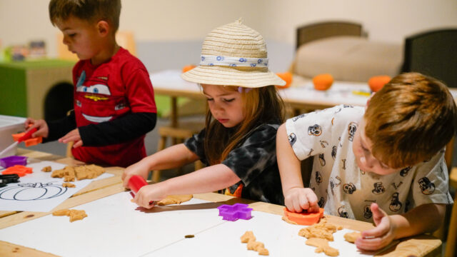 Three children doing a stamping craft on a table. The middle child is wearing a brimmed hat.