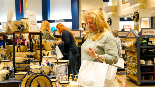 A woman holding a white shopping bag looking at blue bonnet products in the museum store.