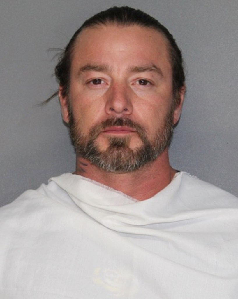 Mugshot of Zackery Dondlinger, a man with brown hair and a beard, wearing a white smock.