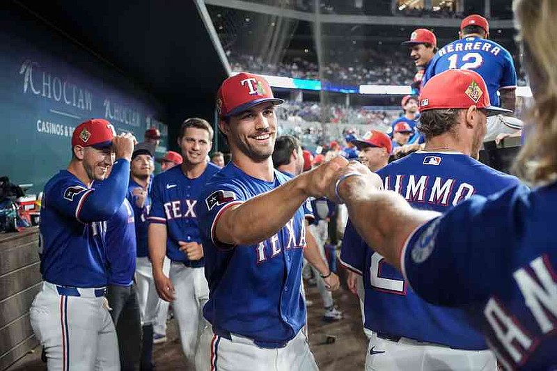 Texas Rangers pitcher Carter Baumler, center, gets a fist-bump in the dugout after he was informed he made the opening day roster during the fifth inning of an exhibition baseball game against the Kansas City Royals, Monday, March 23, 2026, in Arlington., Texas. (Smiley N. Pool/The Dallas Morning News via AP)