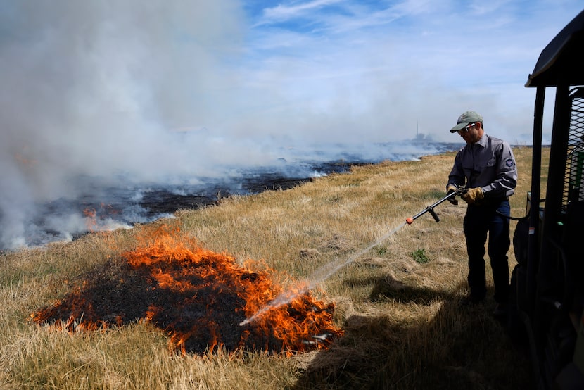 Austin Rollins grabs a pressure sprayer to extinguish a spot fire during a controlled burn...