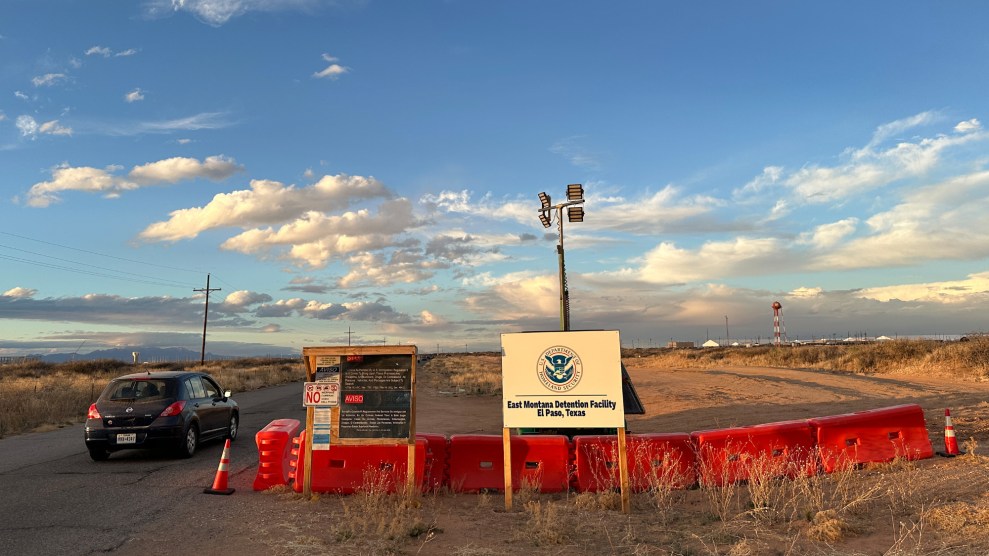 A makeshift wall is set up with a small sign noting the detention facility set in front of a large blue sky and open field.