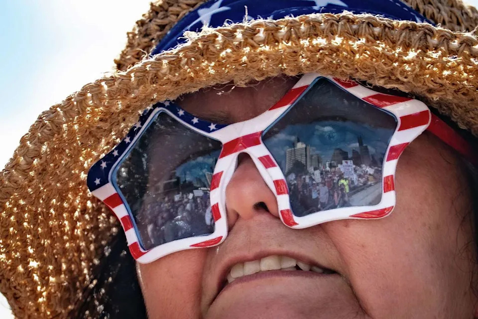 Protesters crossing the First Street bridge are reflected in the sunglasses of a protester watching the crowd go by as thousands march through downtown Austin for the No Kings rally, Oct. 18, 2025. The rally against President Donald Trump and his policies included speakers, a march from the Texas State Capitol to Auditorium Shores and live music and occurred in conjunction with others across the country. (Sara Diggins/Austin American-Statesman)