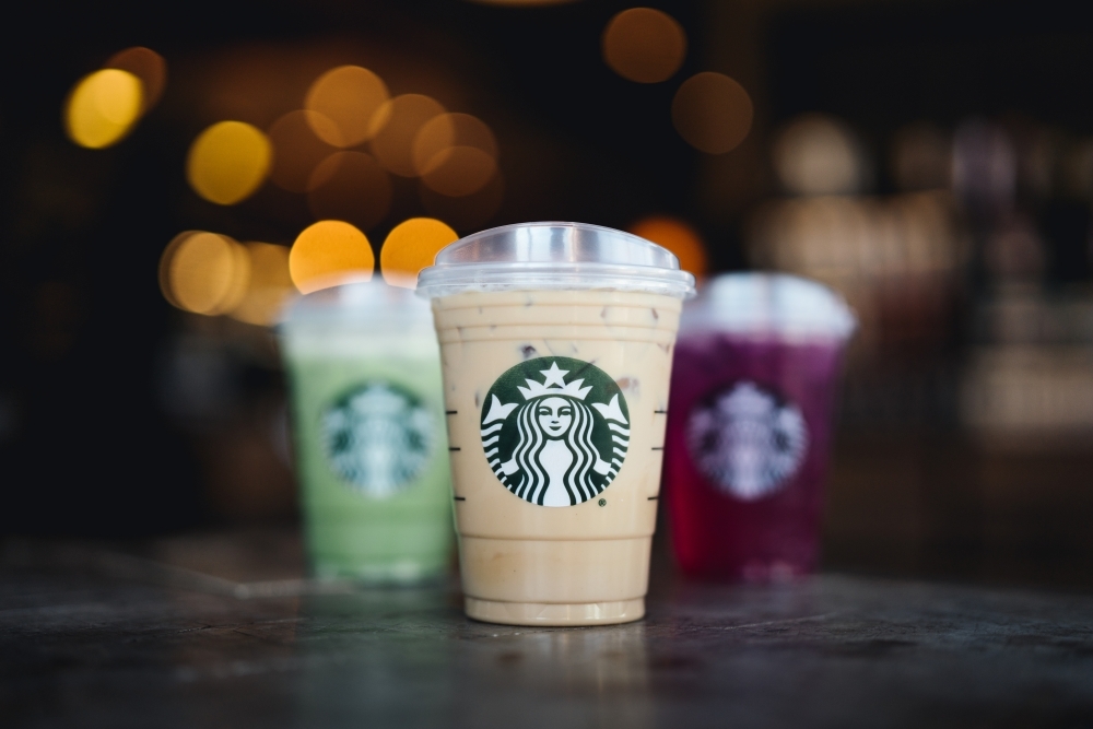 Three clear plastic cups featuring Starbucks logos and filled with three different colored beverages.
