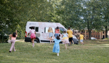 Kids running through green grass on a summer day towards an ice cream truck.